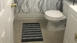 Une salle de bain avec des toilettes, un rideau de douche à motifs ondulés, un tapis rayé noir et blanc et une étagère en métal avec des serviettes.