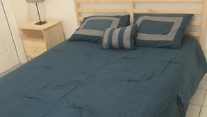 Un lit avec une couvre-lit bleue et deux oreillers, une tête de lit en bois et une table de chevet avec une lampe.