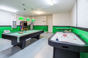 Een biljart tafel met een keu, een tafelvoetbalspel en groene accenten aan de muur.