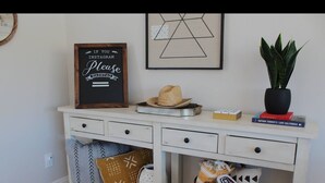 Uma cômoda branca com um quadro negro, um chapéu, uma planta e livros.