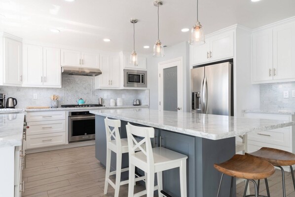 A modern kitchen with white cabinetry, a large island with bar stools, stainless steel appliances, and pendant lighting.