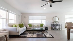 Uma sala de estar ampla com um sofá branco, uma mesa de centro de vidro e um ventilador de teto com moldura preta.