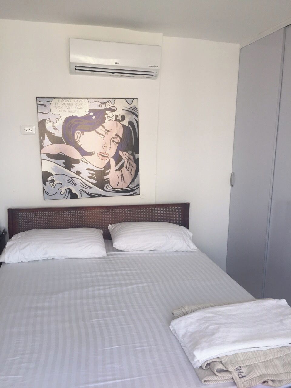 Une chambre d’hôtel avec un lit, deux oreillers, un climatiseur fixé au mur et une grande œuvre d’art représentant une femme dans l’eau.