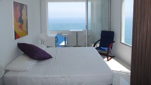 A bedroom with a bed, a chair, a small table, and a view of the sea. - Spacious And Stylish Oceanfront Apartment (Cartagena)