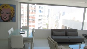 A modern living room with a glass dining table, white chairs, a grey sofa, and a glass coffee table. - Spacious And Stylish Oceanfront Apartment (Cartagena)