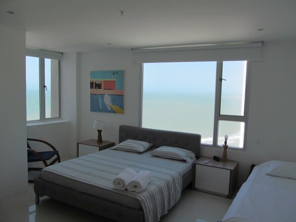 A bedroom with a bed, a chair, a nightstand, and a painting. - Spacious And Stylish Oceanfront Apartment (Cartagena)