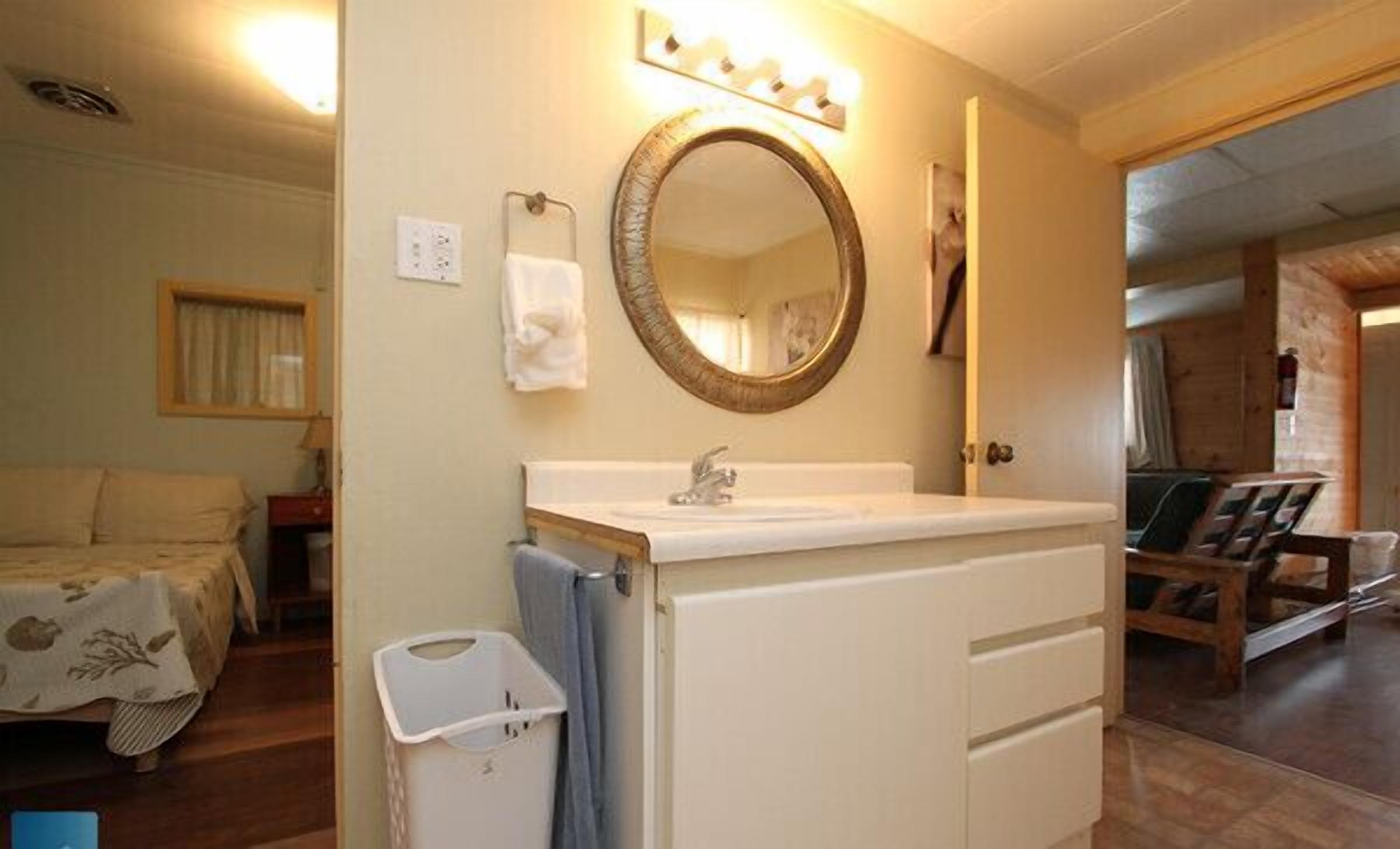 A hotel room with a bed, a bathroom with a sink and mirror, and a wooden floor.