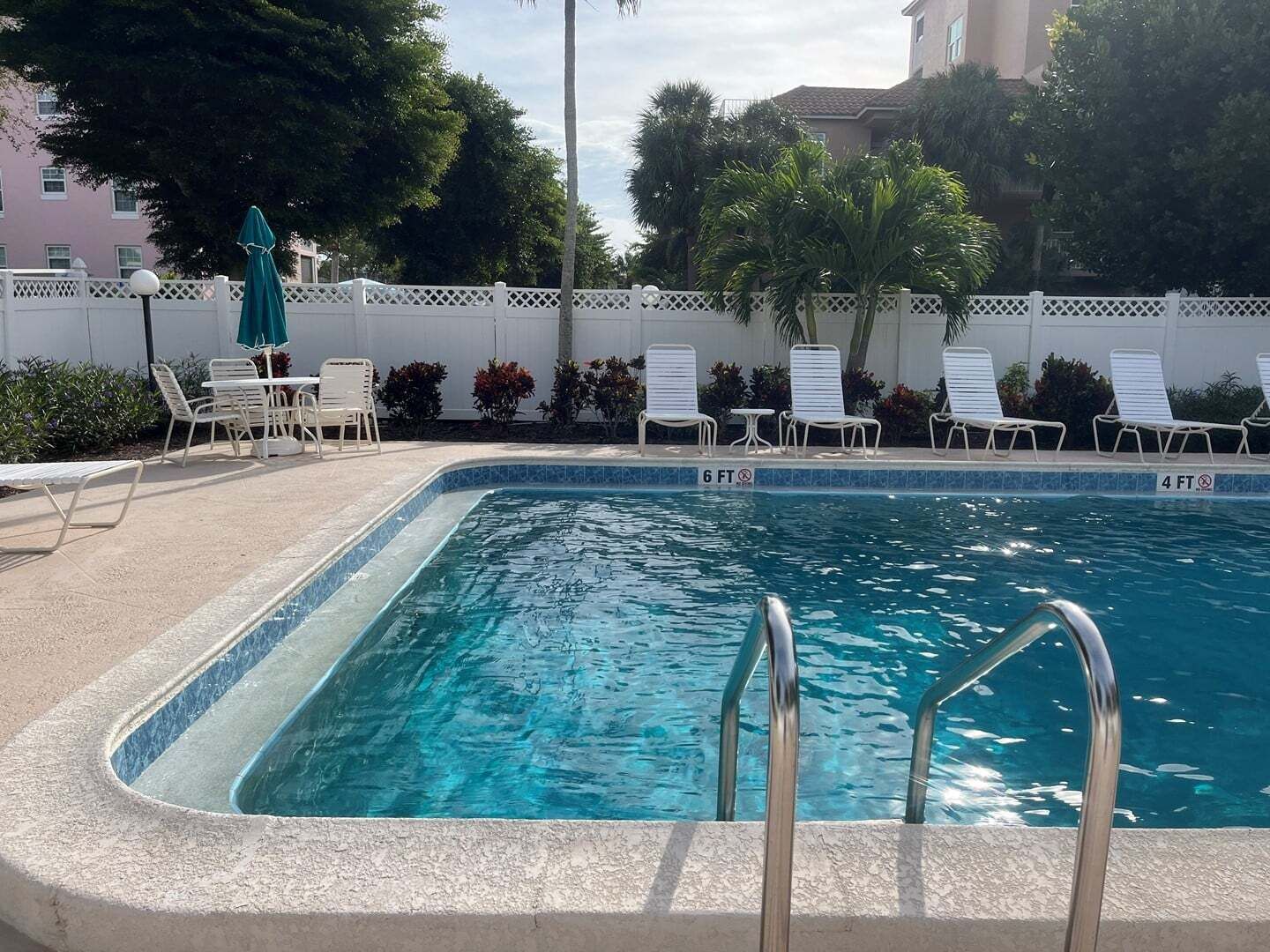 Une piscine dont la profondeur maximale est indiquée à 6 pieds, entourée de chaises longues et délimitée par une clôture blanche.