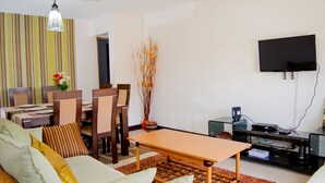 A living room with a sofa, dining table, chairs, a flat-screen TV, and a coffee table.
