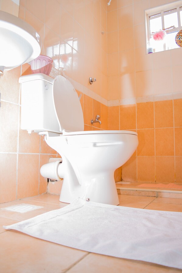 A bathroom with a white toilet, a white sink, and a window with a pink fluffy decoration.