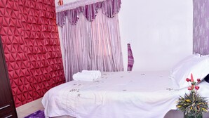 A bedroom with a red geometric wall, a bed with white bedding, and a purple curtain.