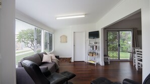 A spacious living room with a grey sofa, black leather chairs, a flat-screen TV, and a wooden bookshelf.