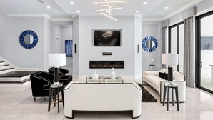 A modern living room with a central white sofa, black and white chairs, a glass coffee table, and a flat-screen TV mounted above a fireplace. - The White House Of Reunion (Orlando)