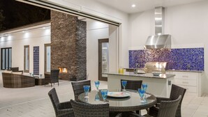 A modern outdoor dining area with wicker furniture and blue glassware, a stone pillar, and a kitchen with blue-tiled backsplash and stainless steel appliances. - The White House Of Reunion (Orlando)