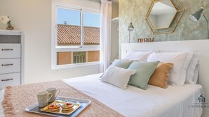 Ein Schlafzimmer mit einem Bett, einem Nachttisch, einem Fenster und einer Wand mit einem geometrischen Spiegel und dem Schriftzug 'DREAM'.