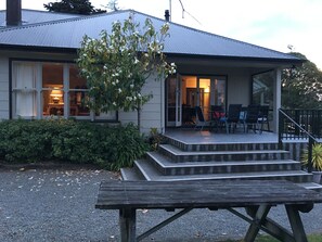 Een huis met een overdekte veranda, een houten bankje en een boom ervoor.
