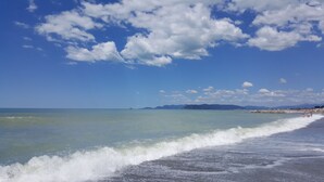 A beach with clear blue water, waves, and distant mountains under a partly cloudy sky. - Casale Amati Il Frantoio, near Cinque Terre. (ortonovo)