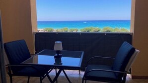 Un balcón con una mesa de vidrio y dos sillas, con vista al mar azul y despejado.