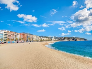 Una playa con una hilera de edificios coloridos a lo largo de la orilla, cielo azul despejado y olas marinas tranquilas.