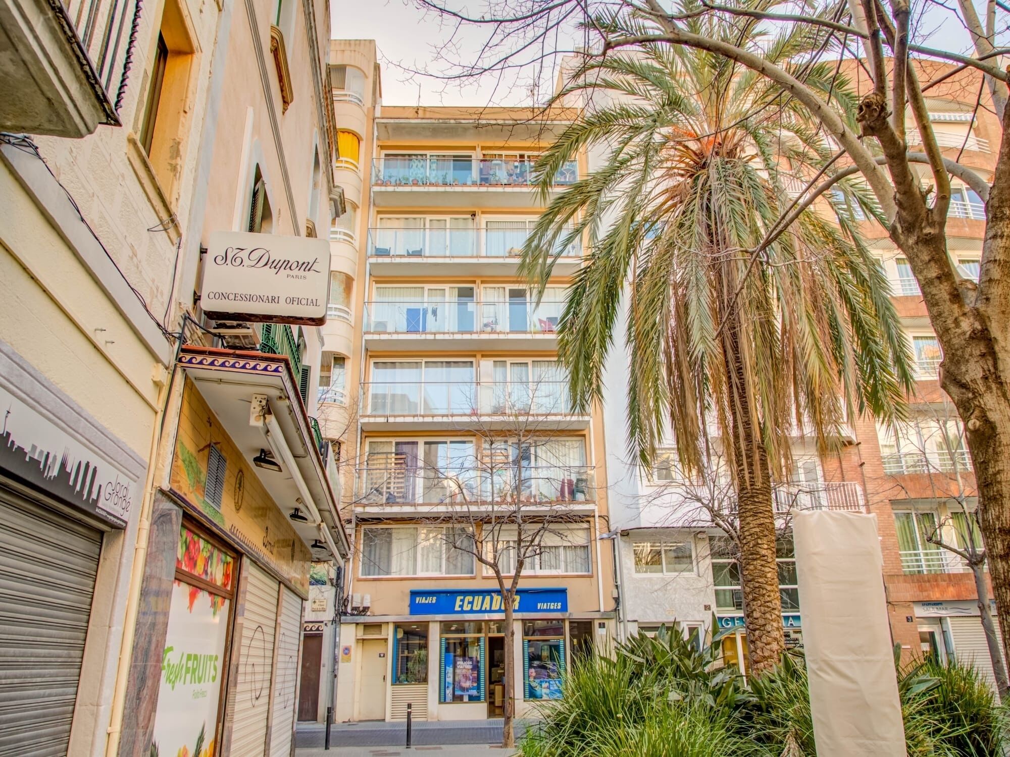 A multi-story building with balconies, a fruit shop, and a travel agency.