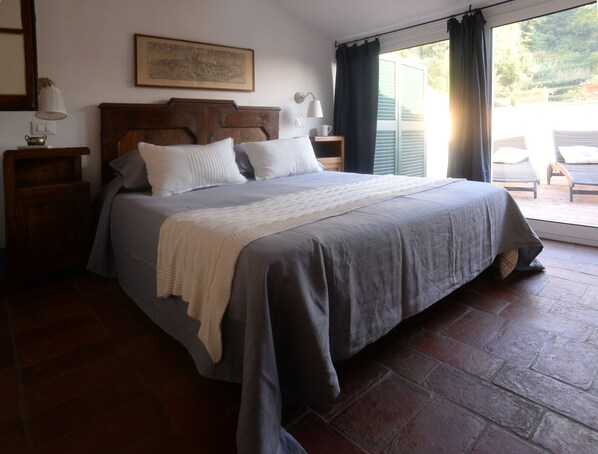 A bedroom with a large bed, a wooden headboard, a nightstand with a lamp, and a view of the outdoors through a sliding door.