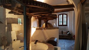 Un interior rústico con un molino de piedra, una ventana con vistas y un sofá tradicional.