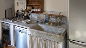 Una cocina con estufa a gas, un lavamanos con grifo, un escurreplatos y un armario con vajilla.