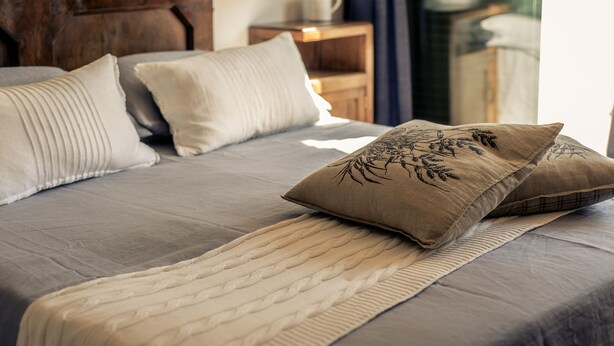 Una cama bien hecha con un edredón gris, almohadas color beige y marrón, y una manta color beige.