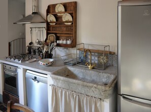 A kitchen with a gas stove, a sink with a faucet, a dish rack, and a cabinet with dishes.
