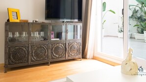 A living room with a television on a cabinet, a glass cabinet with wine glasses, and a view of a garden through a sliding door. - Atarazanas Executive Living4malaga (M��laga ciudad)