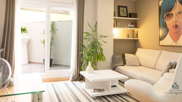 A modern living room with a sofa, coffee table, and a bookshelf. There is a sliding glass door leading to an outdoor area with plants. - Atarazanas Executive Living4malaga (M��laga ciudad)