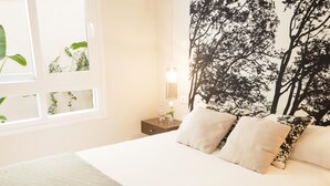 A bedroom with a bed, pillows, a nightstand, a wall-mounted lamp, and a window with plants. - Atarazanas Executive Living4malaga (M��laga ciudad)
