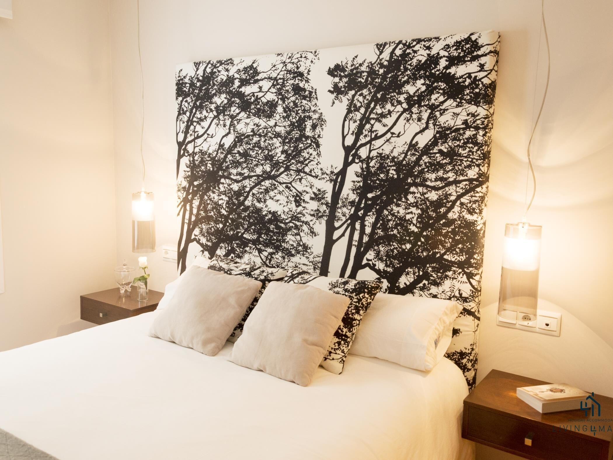 Un dormitorio con una cama grande, dos mesitas de noche y una lámpara fijada a la pared.