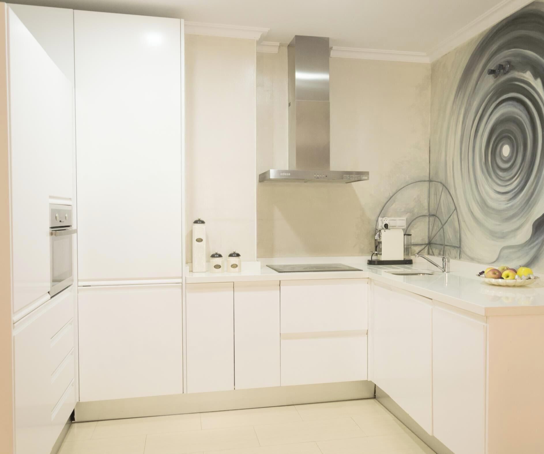Una cocina moderna con armarios blancos, una campana extractora de acero inoxidable, un horno empotrado y una cafetera.