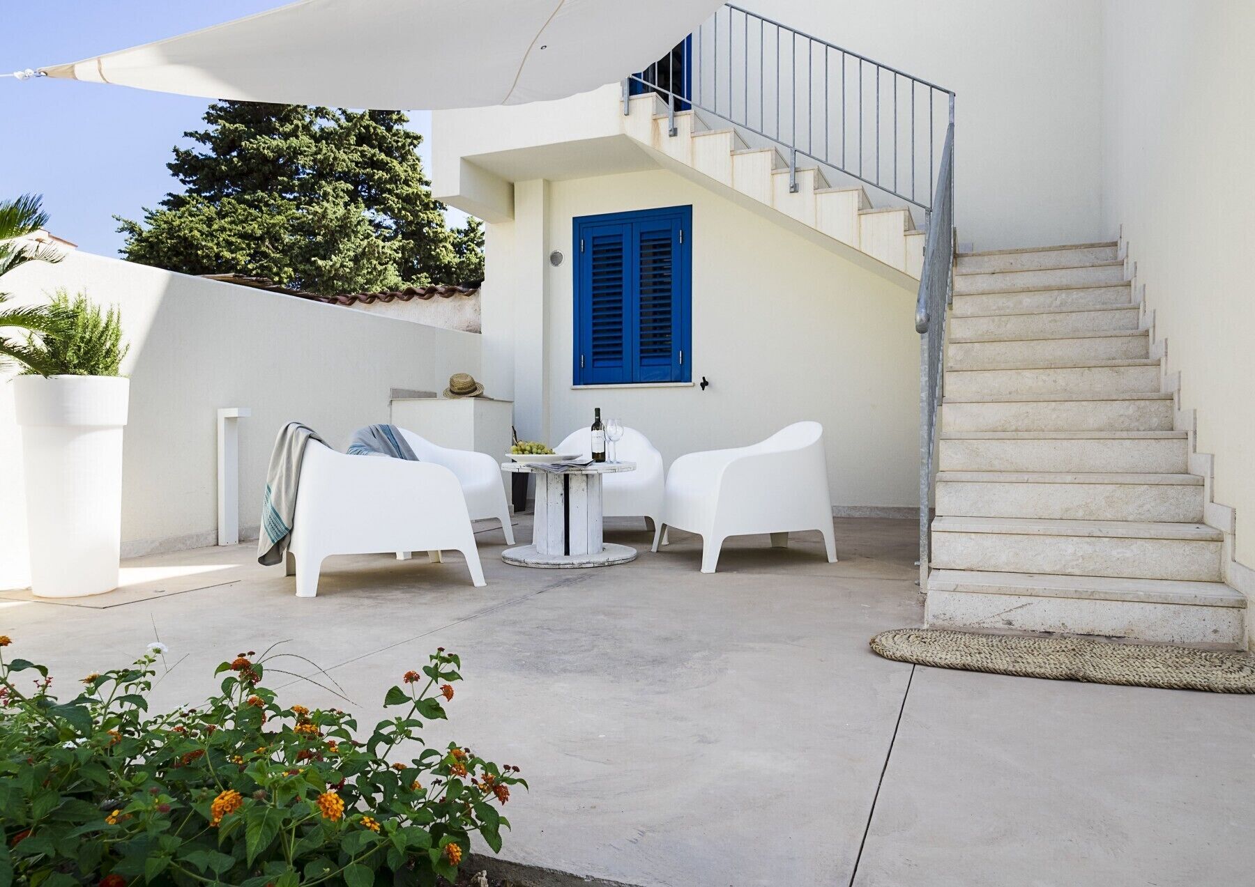 Een modern terras buiten met witte meubels, een blauwe deur en een trap.