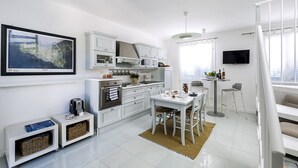 Cozinha moderna com armários brancos, área de refeições com mesa e cadeiras, um pequeno balcão e uma TV na parede.