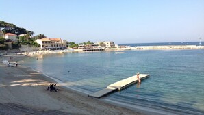 A beach with a wooden pier extending into the water, a sandy shore, and buildings in the background. - Seaside Villa Apartment with Large Terrace  2 mins from Renecros Beach (Bandol)