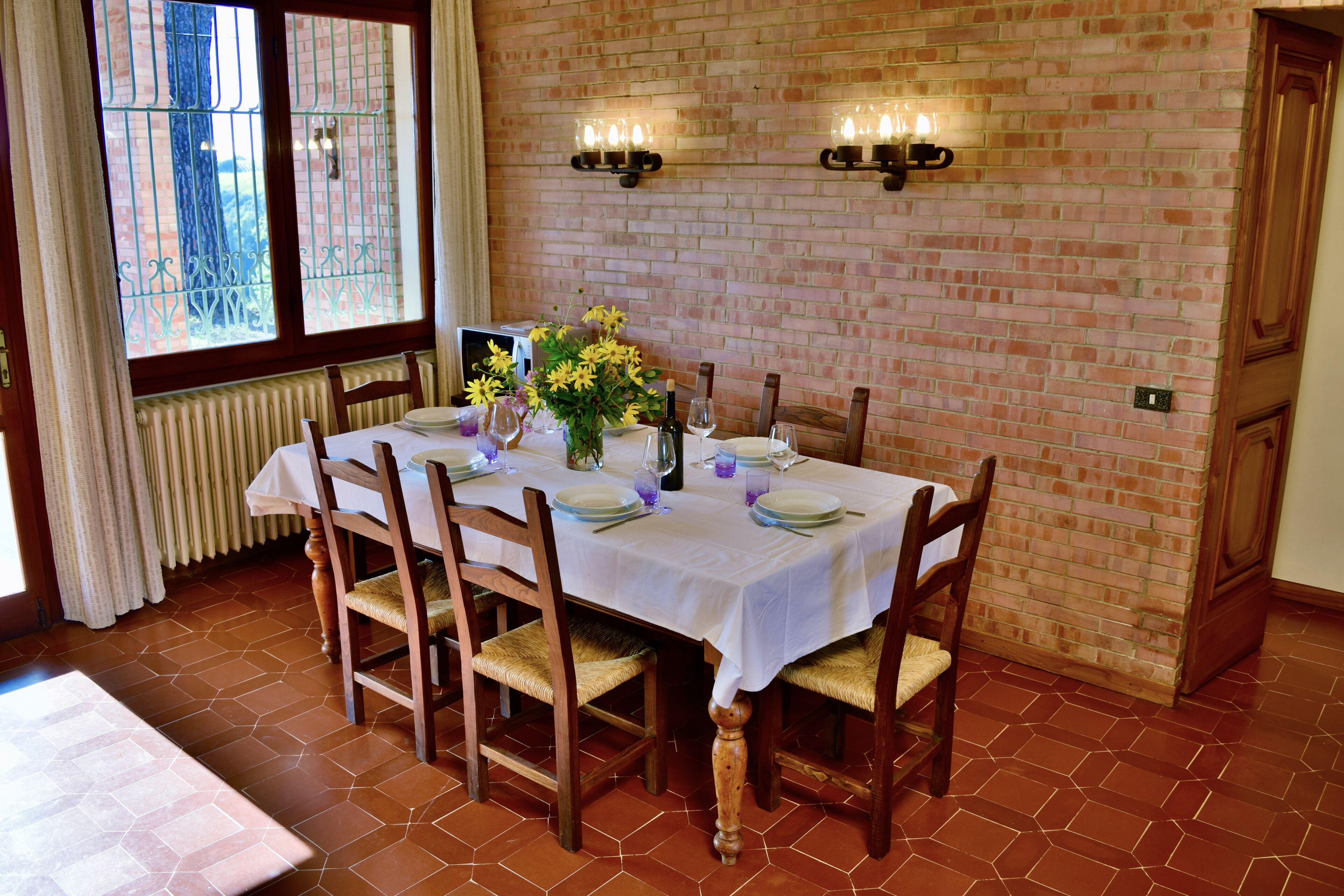 A dining area with a brick wall, a table set for four, and a window with curtains.