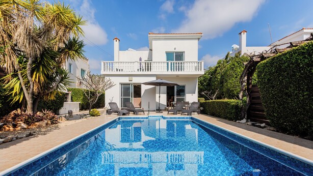 Una piscina con un diseño de mosaico azul claro, rodeada de un patio pavimentado con sillas de descanso.