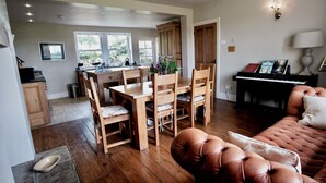Een ruime woonkamer met een houten eettafel, zachte stoelen, een leren bank en een piano.