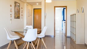 A modern dining area with a glass table, white chairs, and a wooden door in the background. - ApartUP Patacona Orchard (Alboraya)