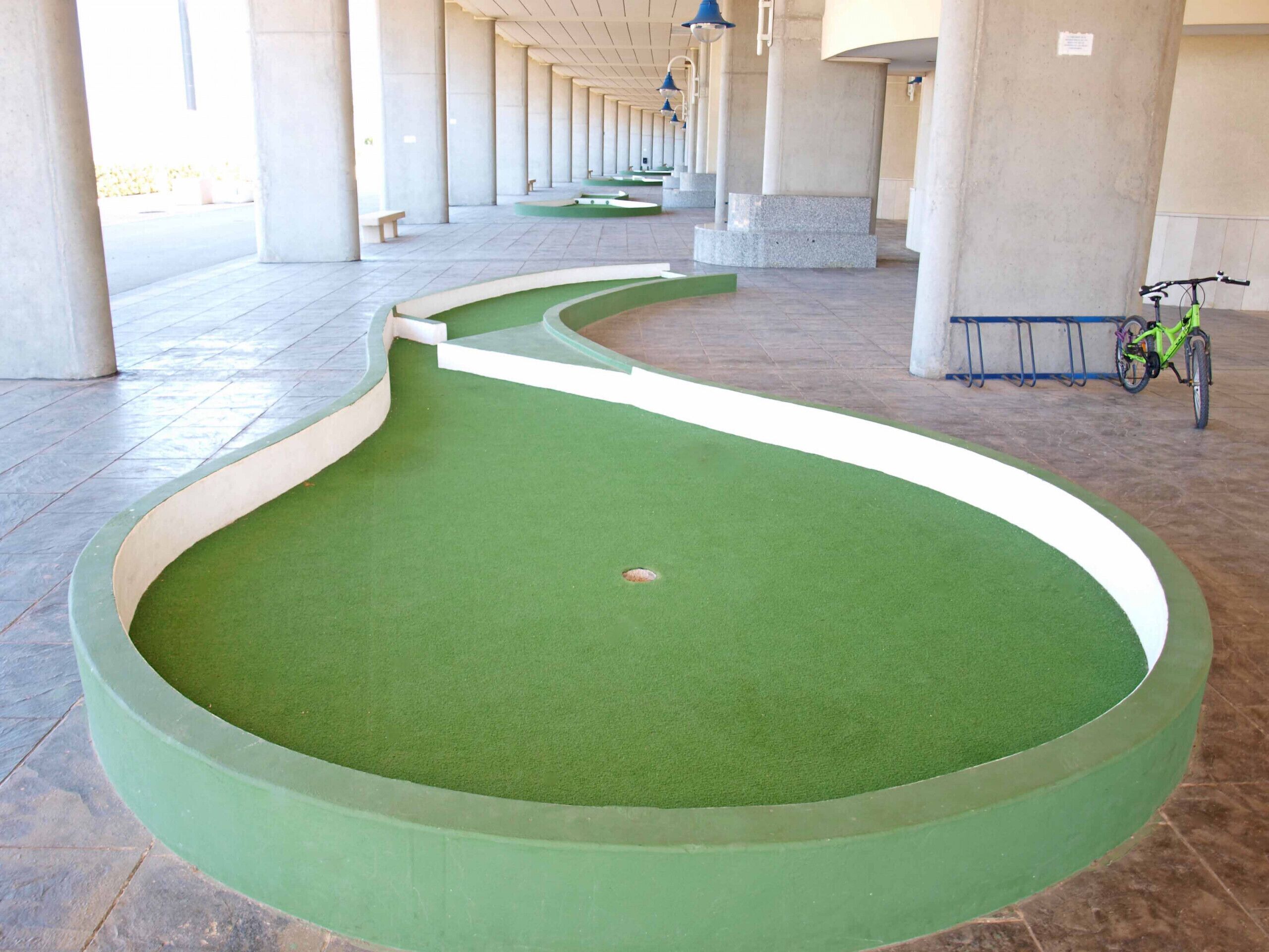 Ein grünes, künstliches Putting-Green mit einem in der Nähe abgestellten Fahrrad.