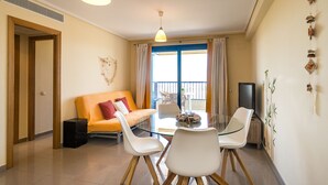 A modern living room with a glass dining table, white chairs, a sofa, and a television. - ApartUP Patacona Orchard (Alboraya)