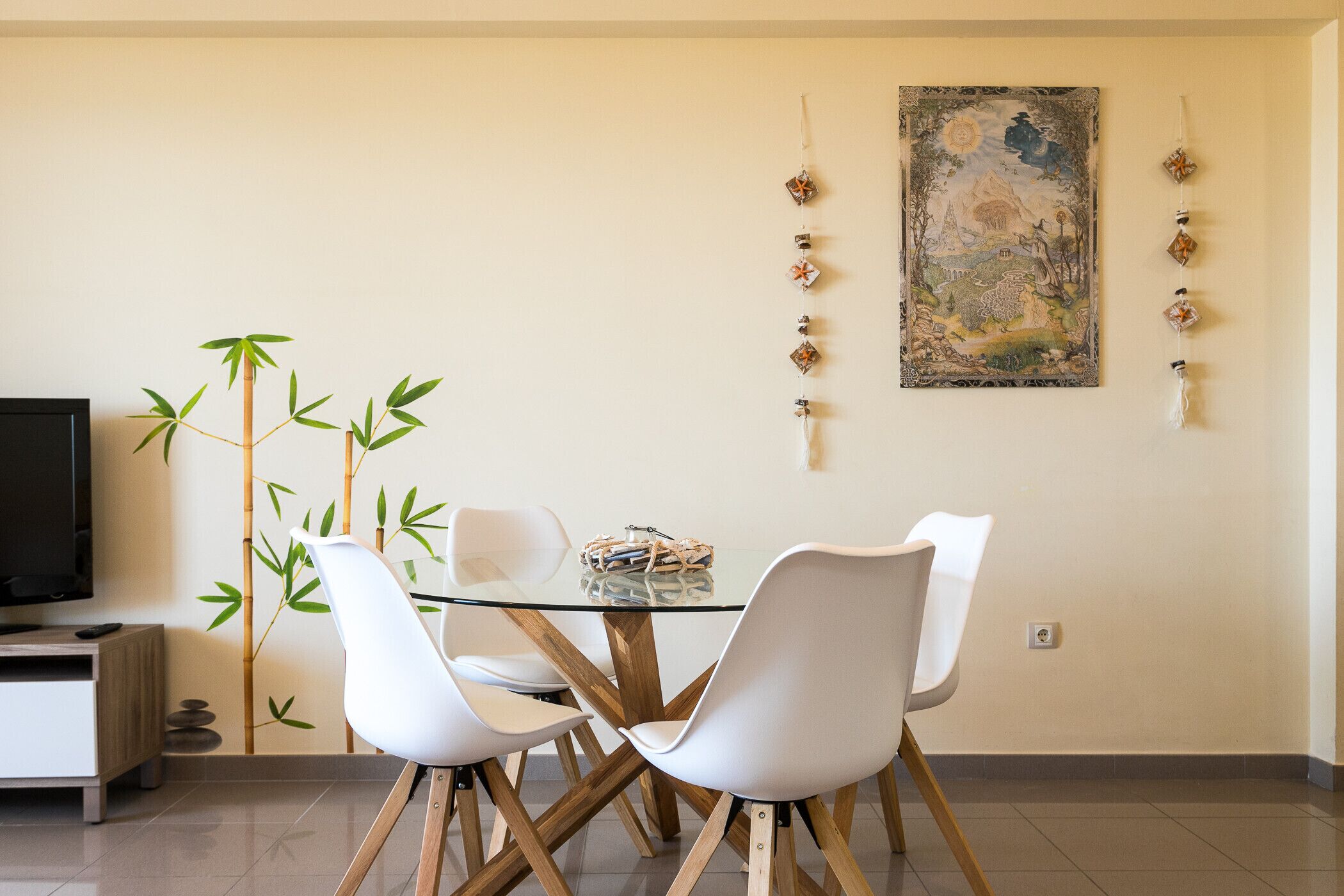 A dining area with a glass table, white chairs, a television, and a bamboo plant.