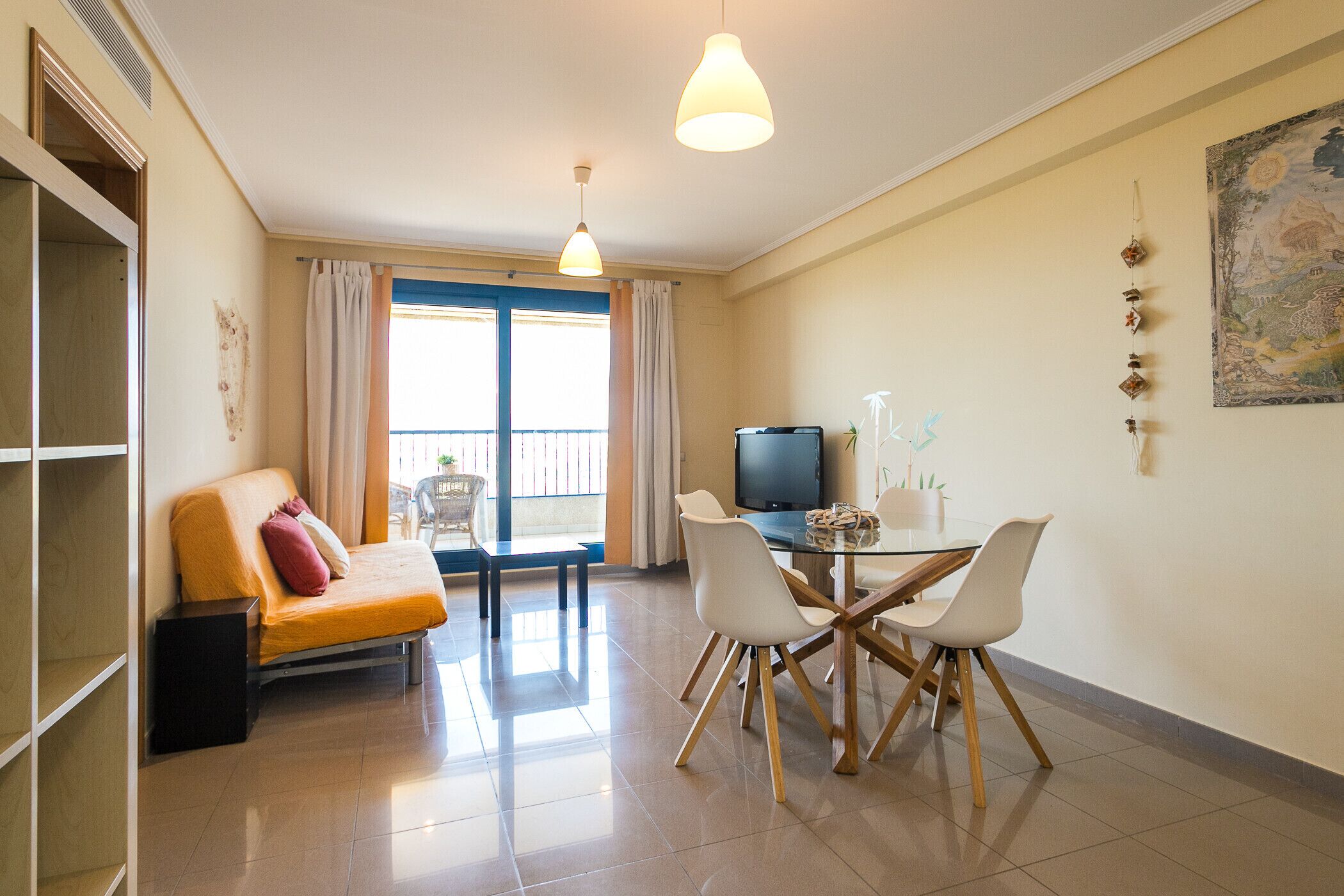 Una sala de estar moderna con sofá, una mesa de comedor con sillas, televisor y balcón con cortinas.