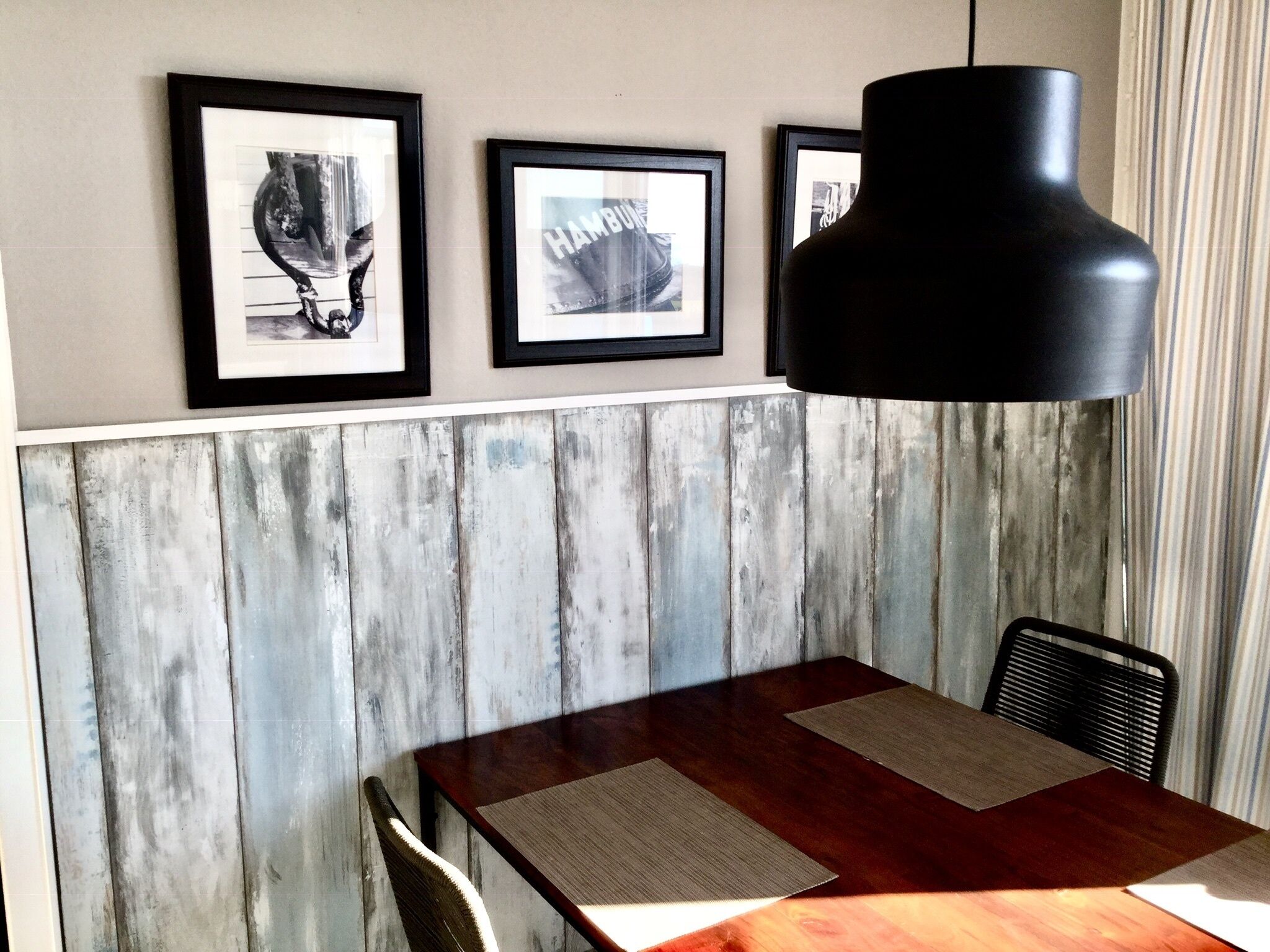 A dining area with a wooden table, framed pictures on the wall, and a black pendant light.