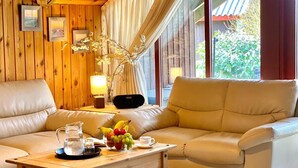 A cozy room with wooden walls, a large window with curtains, a sofa, a coffee table with fruit, and a lamp. - Holidays with child and dog in Gartow am See (Gartow)
