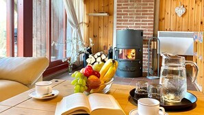 A cozy cabin interior with a wooden dining table set with fruits, a book, and cups. A fireplace and a coffee maker are visible in the background. - Holidays with child and dog in Gartow am See (Gartow)