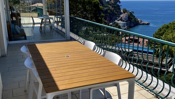Ein Holztisch und Stühle auf einem Balkon mit Blick auf das Meer und eine felsige Küste.