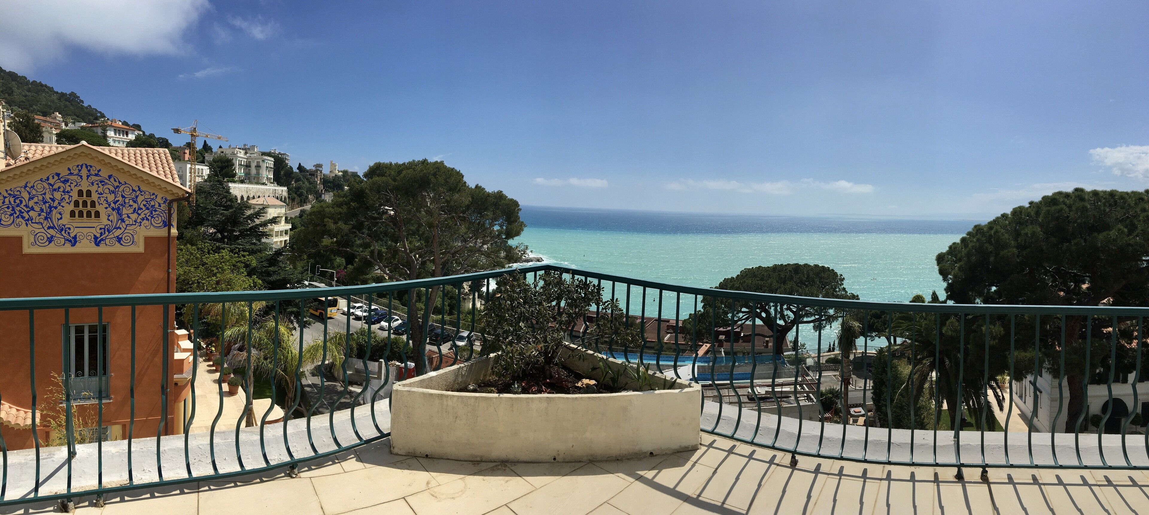 Een balkon met uitzicht op zee, een zwembad en omliggende gebouwen.